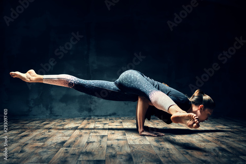 Young woman practicing yoga doing hurdler pose in dark room