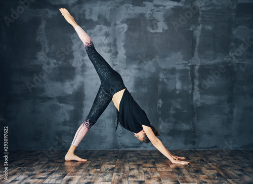 Young sporty woman practicing yoga, doing one legged downward facing dog pose on dark background photo