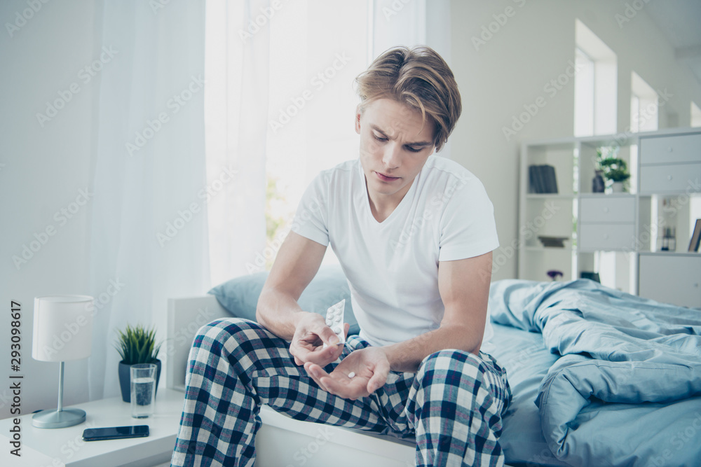 Portrait of unhappy sad male student have terrible headache migraine suffer from cold influenza want have antibiotics vitamins sit oin bed house indoors wear checkered plaid pajama Portrait of unhappy sad male student have terrible headache migraine suffer from cold influenza want have antibiotics vitamins sit oin bed house indoors wear checkered plaid pajama