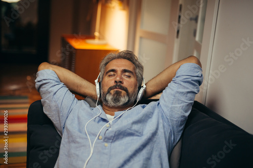 middle aged man listening music on headphones at his home