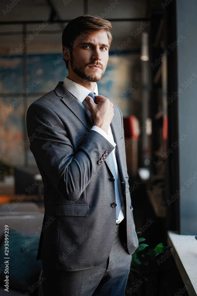 Stylish young bearded man in a suit is standing near the window and looking  far Stock-Foto | Adobe Stock