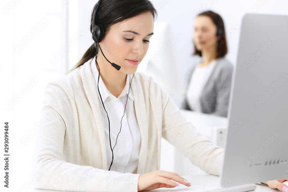Call center. Beautiful woman receptionist sitting in headset at customer service office. Group of operators at work. Business concept Call center. Beautiful woman receptionist sitting in headset at customer service office. Group of operators at work. Business concept