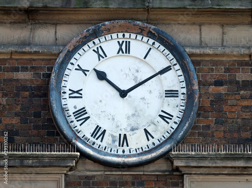 old round clock on the brick wall of a building with roman numerals with hands at ten past ten