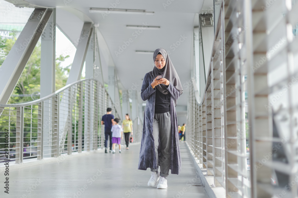 Beautiful muslim woman walking and using telephone phone in city.