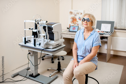 Senior woman checking vision with eye test glasses during a medical examination at the ophthalmological office