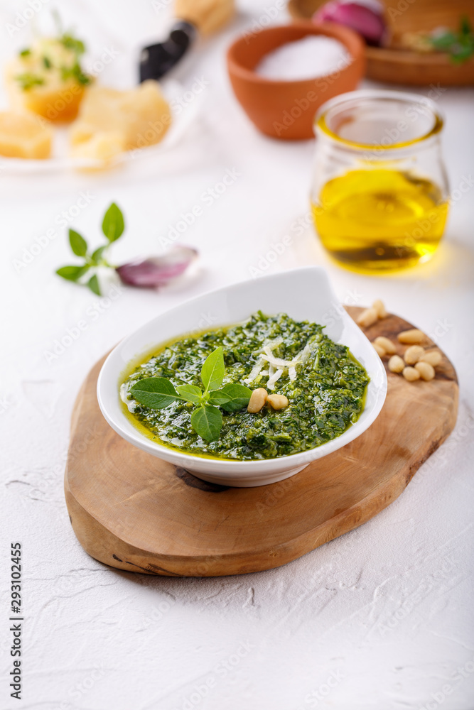 Pesto sauce with some ingredients - basil, olive oil, pine nuts, parmesan and garlic - on white table. Pesto sauce with some ingredients - basil, olive oil, pine nuts, parmesan and garlic - on white table.