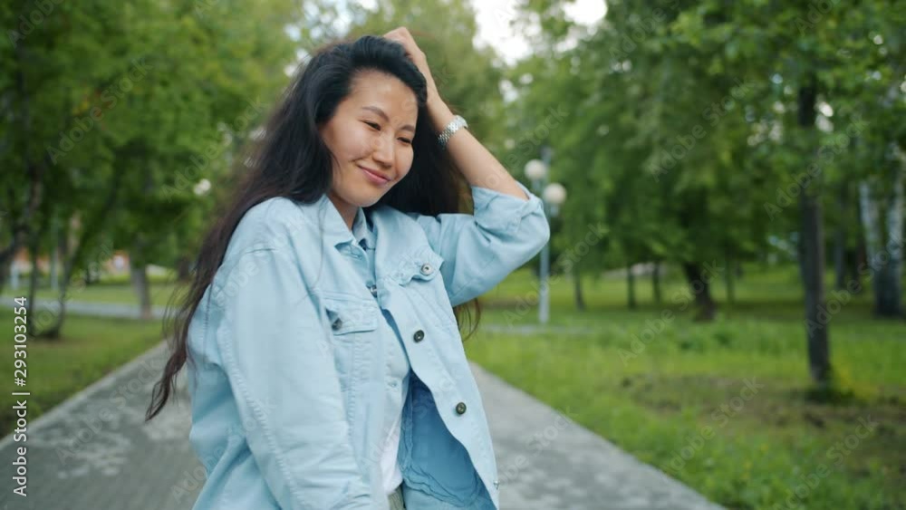 Rear view of beautiful Asian lady walking in park alone then turning to camera smiling with happy face. Modern lifestyle, people and casual life concept. Rear view of beautiful Asian lady walking in park alone then turning to camera smiling with happy face. Modern lifestyle, people and casual life concept.
