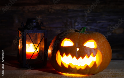 an old lantern and halloween pumpkin with carved eyes and a scary smile glowing in darkness, close up