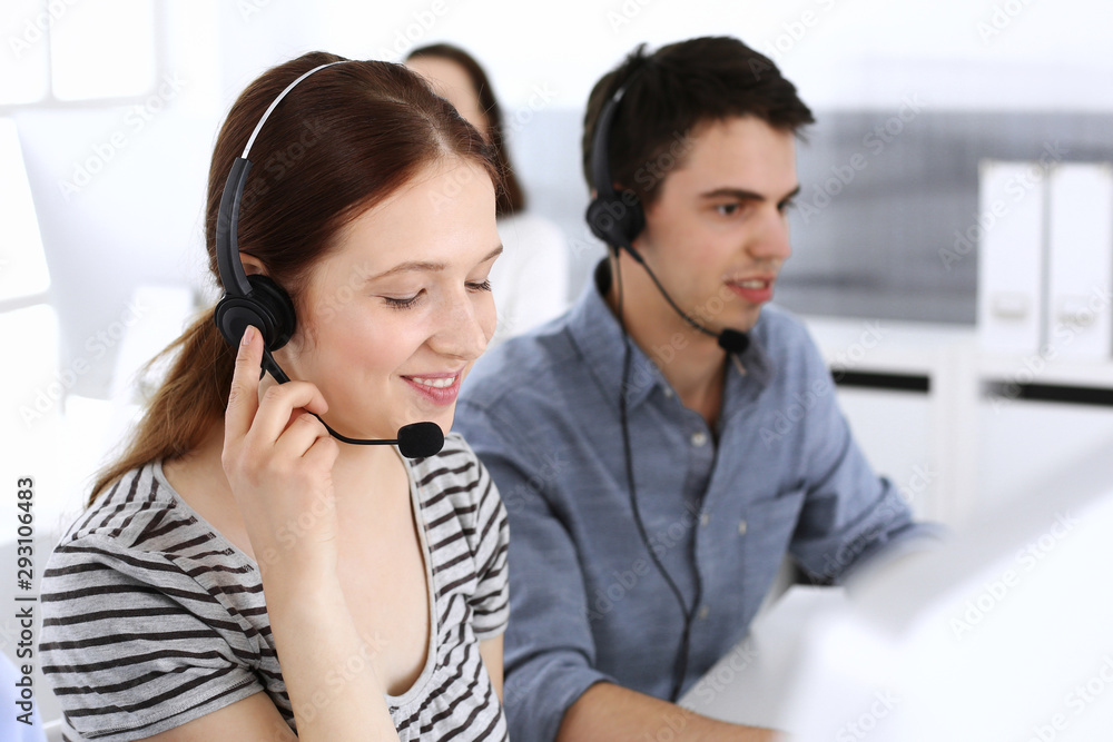 Group of operators at work. Call center. Focus on beautiful woman receptionist in headset at customer service. Business concept and casual striped clothing style Group of operators at work. Call center. Focus on beautiful woman receptionist in headset at customer service. Business concept and casual striped clothing style