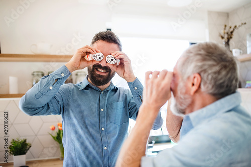 A portrait of adult hipster son and senior father indoors at home, having fun.