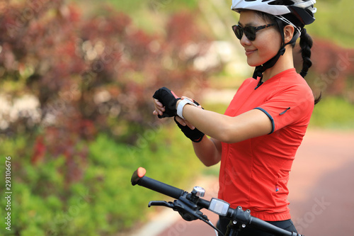 Woman cyclist looking at her smartwatch while riding bike on sunny day