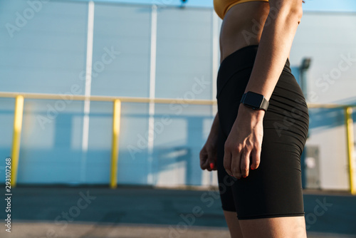 Cropped image of woman in sportswear standing with wristwatch outdoors