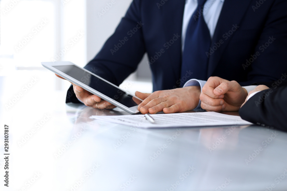 Business people using tablet computer while working together at the desk in modern office. Unknown businessman or male entrepreneur with colleague at workplace. Teamwork and partnership concept Business people using tablet computer while working together at the desk in modern office. Unknown businessman or male entrepreneur with colleague at workplace. Teamwork and partnership concept