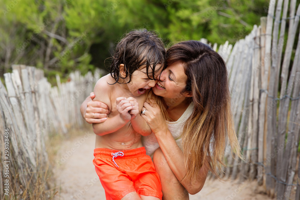 Mother and son cuddling and laughing together on sandy path at beach Mother and son cuddling and laughing together on sandy path at beach