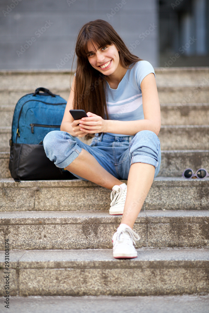 Full body young woman sitting on steps with mobile phone and bag Full body young woman sitting on steps with mobile phone and bag