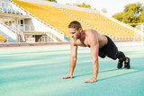 Image of strong shirtless man doing plank exercise at sports stadium