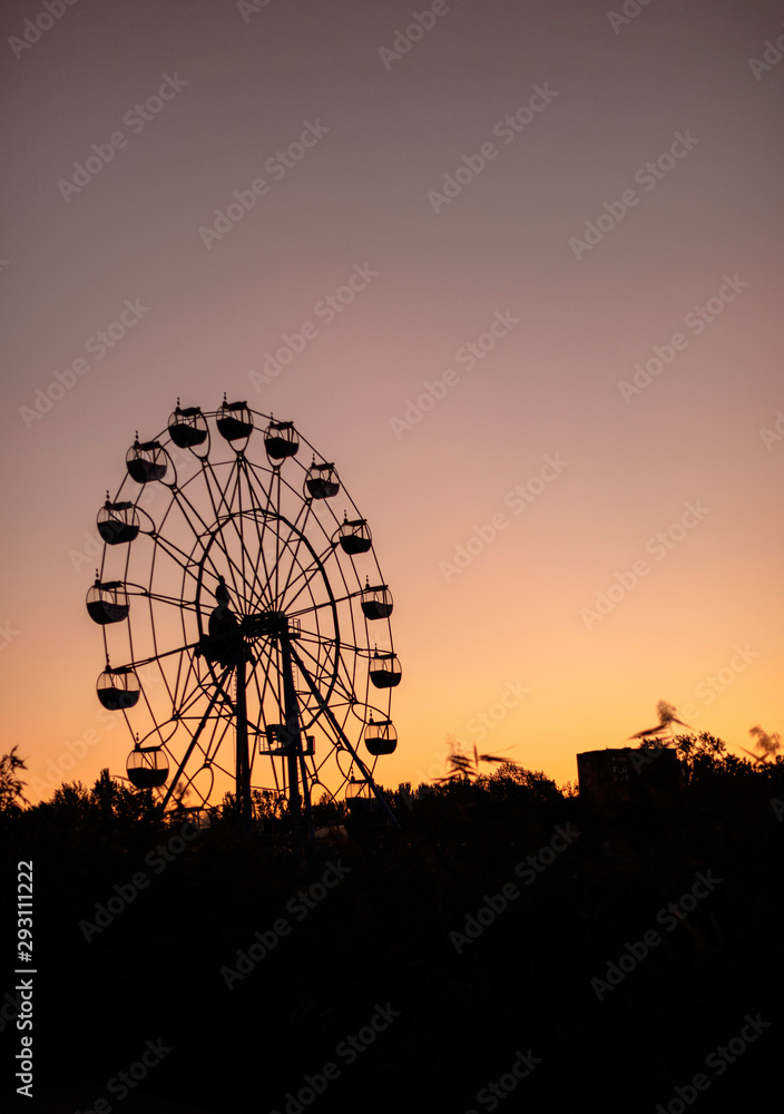 Silhouette of a ferris wheel at sunrise (sunset) of the sun on a background of trees and grass. Silhouette of a ferris wheel at sunrise (sunset) of the sun on a background of trees and grass.