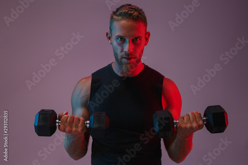 Concentrated young sports man make exercises with dumbbells.