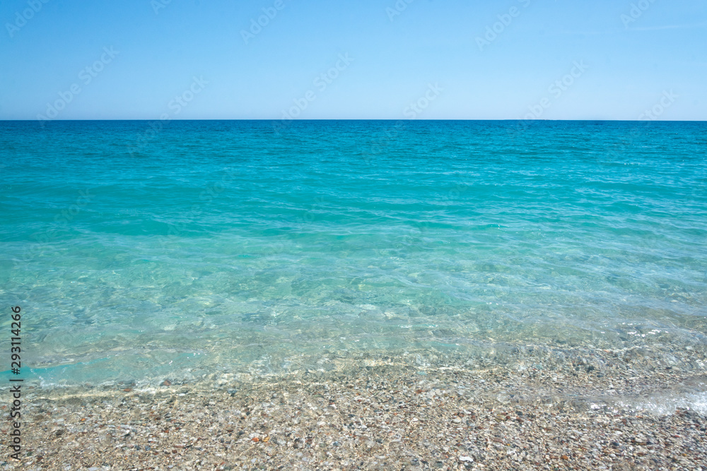 Turquoise sea, slightly rocky beach, mountains in the distance Turquoise sea, slightly rocky beach, mountains in the distance