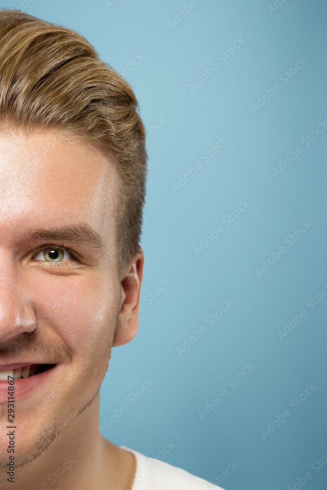 Fototapeta premium Caucasian young man's close up portrait on blue studio background. Beautiful male model with well-kept skin. Concept of human emotions, facial expression, sales, ad, beauty. Smiling, laughting.