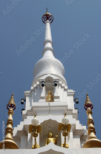 The top of a white stupa at a temple housing sacred gold relics associated with the Buddha against a blue sky background