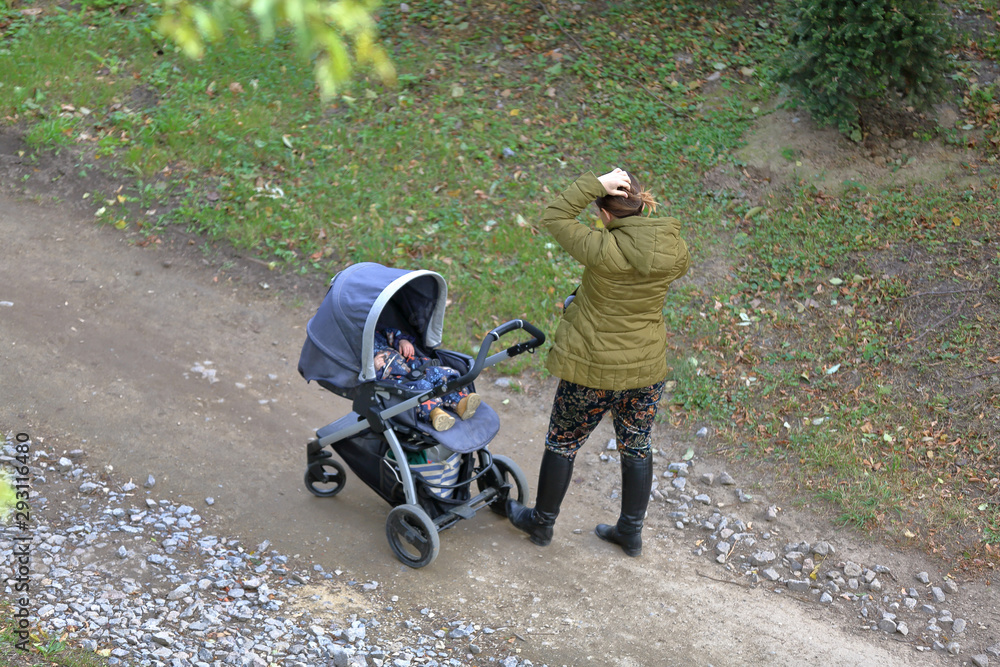 Obraz premium Woman with a baby stroller walks through the the picturesque autumn park