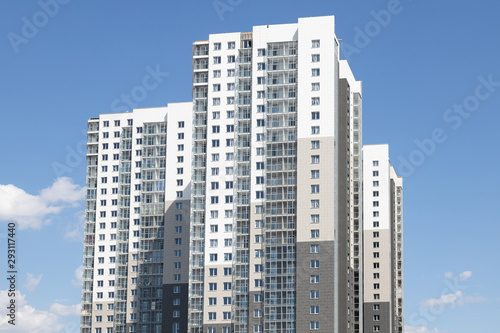 High white-grey multi-family dwelling building against blue sky