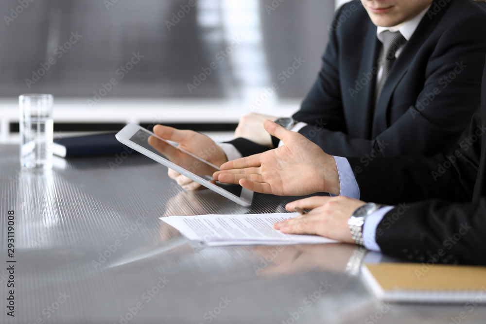 Businessman using tablet computer and work together with his colleague or partner at the glass desk in modern office, close-up. Unknown business people at meeting. Teamwork and partnership concept Businessman using tablet computer and work together with his colleague or partner at the glass desk in modern office, close-up. Unknown business people at meeting. Teamwork and partnership concept