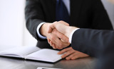 Businessman shaking hands with his colleague or partner above the glass desk in modern office, close-up. Unknown business people at meeting. Teamwork, partnership and handshake concept