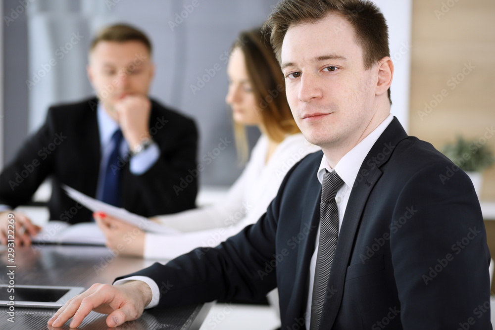 Businessman headshot at meeting in modern office. Unknown entrepreneur sitting with colleagues at the background. Teamwork and partnership concept Businessman headshot at meeting in modern office. Unknown entrepreneur sitting with colleagues at the background. Teamwork and partnership concept