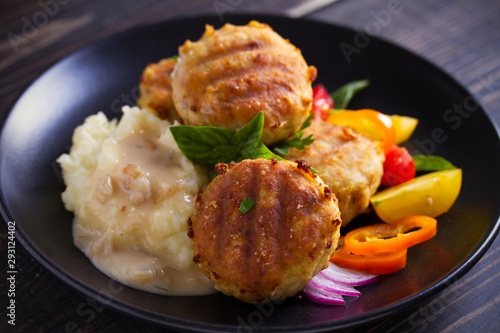 Fish cakes with mashed potatoes and vegetables, garnished with basil. Fish burgers on black table. Horizontal image