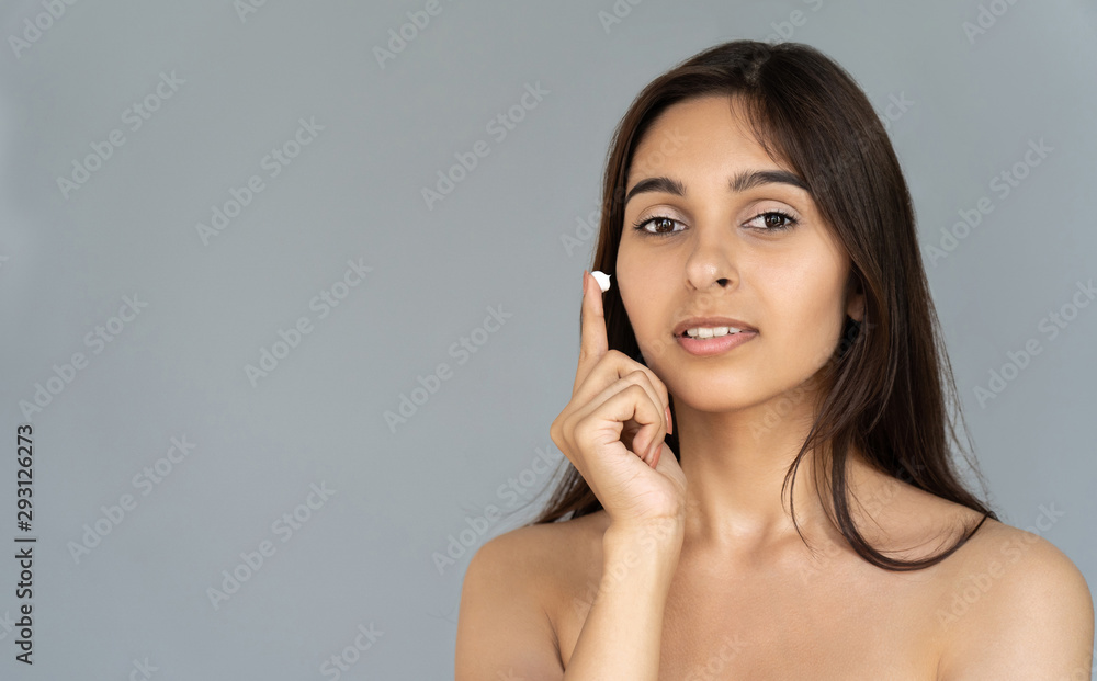 Young attractive woman girl apply cream on face look at camera isolated on grey studio background, facial cosmetic spa skin care concept, natural beauty cosmetology advertisement, copy space portrait Young attractive woman girl apply cream on face look at camera isolated on grey studio background, facial cosmetic spa skin care concept, natural beauty cosmetology advertisement, copy space portrait