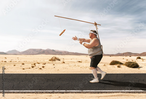 Funny overweight man chasing the hot dog on the stick through the empty road with copy space photo