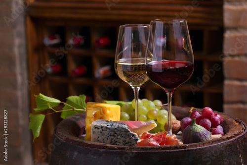Red and white wine with  grapes on old cask in wine cellar. Glasses and bottles of wine with cheese  jamon  figs and nuts