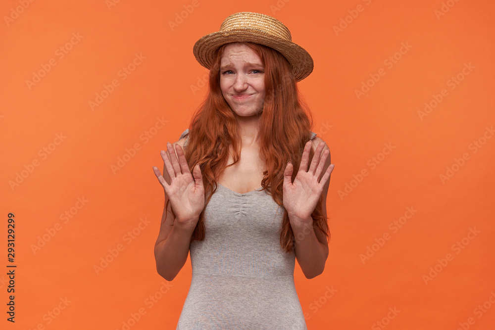 Portrait of pretty young foxy haired female posing over orange background in casual clothes, raising palms in refusing gesture, frowning and pursing lips Portrait of pretty young foxy haired female posing over orange background in casual clothes, raising palms in refusing gesture, frowning and pursing lips