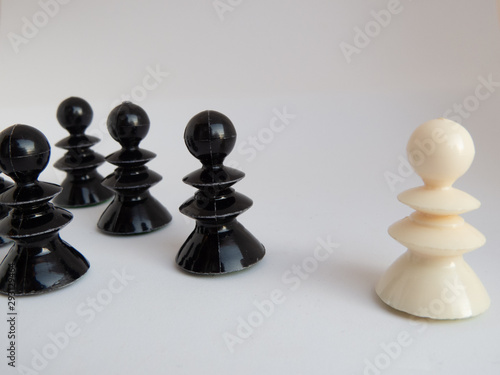 One white chessman standing opposite of a group of black chess pieces