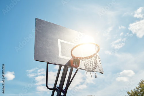 Photo of basketball hoop against blue, cloudy sky on summer day.