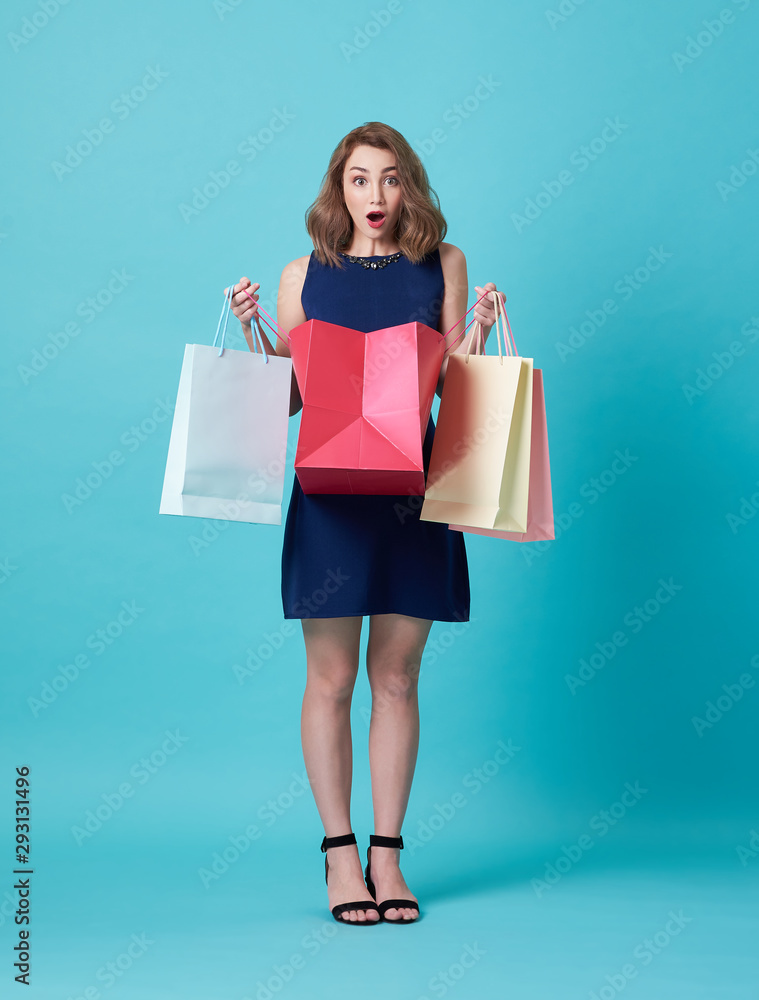 Happy beautiful young woman in blue dress and hand holding shopping bag isolated over blue background.