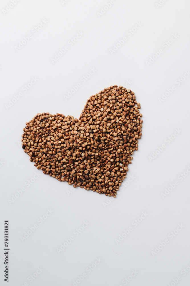 Raw buckwheat on white background shaped as heart symbol and tape measure Raw buckwheat on white background shaped as heart symbol and tape measure