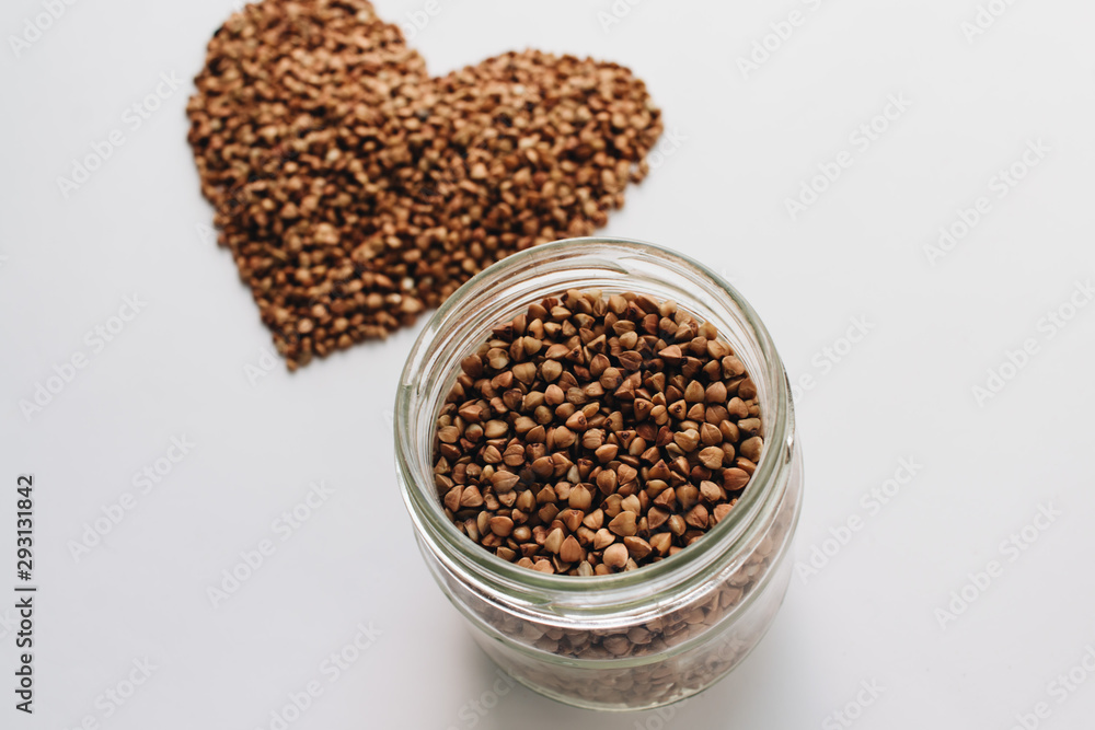 Raw buckwheat on white background shaped as heart symbol and tape measure Raw buckwheat on white background shaped as heart symbol and tape measure