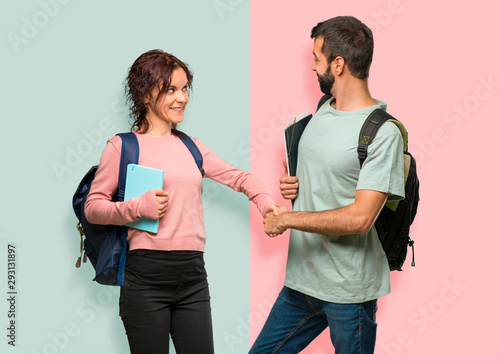 Two students with backpacks and books shaking hands for closing a good deal on colorful wall