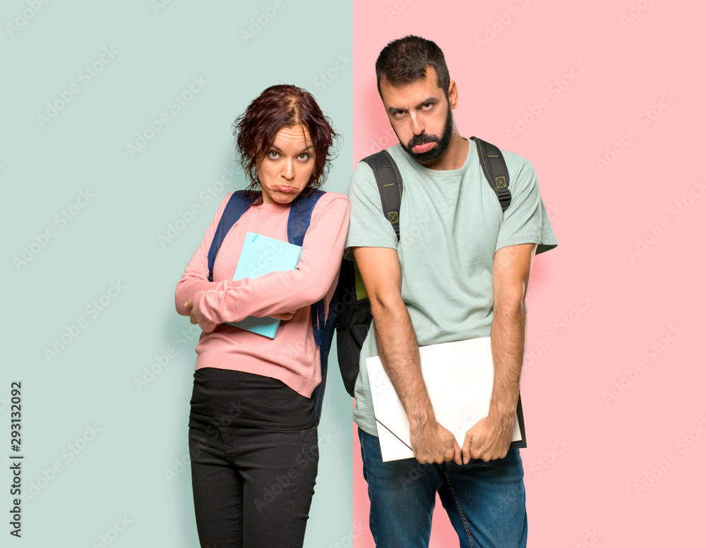 Two students with backpacks and books with sad and depressed expression. Serious gesture on colorful wall Two students with backpacks and books with sad and depressed expression. Serious gesture on colorful wall