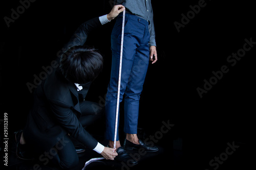 The dressmaker was using a tape measure to measure the length of the leg on a black background.
