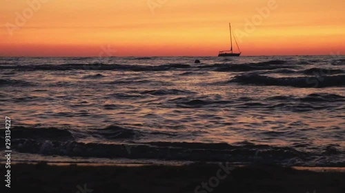 Red-orange sunset on the sea with a prominent sailing yacht on the horizon. Bright colors of sea sunset.