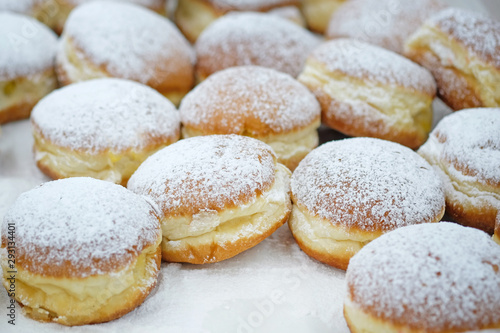 Homemade stuffed donuts on a parchment covered table. Round donuts sprinkled with white icing sugar with fruit jam. Sweet baking department in the store.