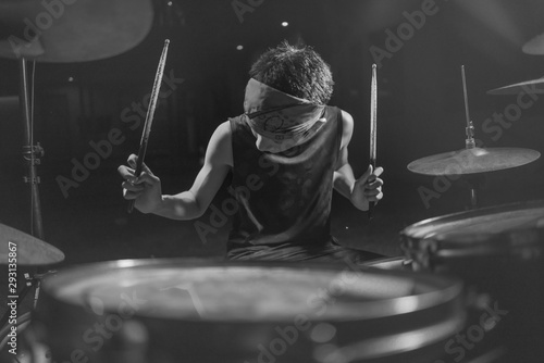 Teenager rock band drummer . cool and talented Asian American mixed ethnicity teenage boy playing drums in headband performing song in dark foggy stage