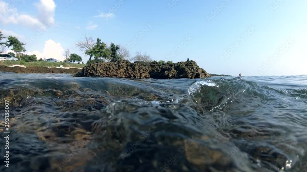 Slow motion tidal wave hitting rock shore, alternating view above water and underwater