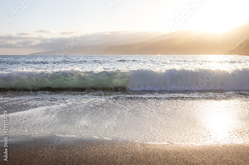 Breaking wave at sunrise. Sandy beach, Canary Islands.