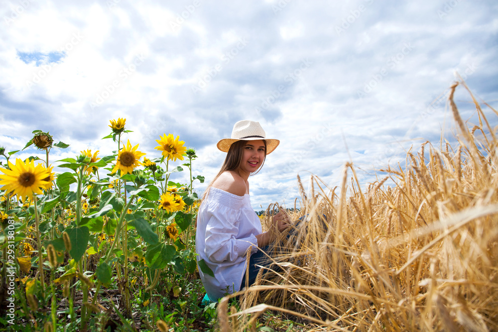 Brunette woman in white blouse sitting on a background of golden wheat and sunflowers fields Brunette woman in white blouse sitting on a background of golden wheat and sunflowers fields