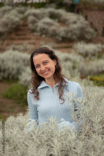 Portrait of young woman wearing blue gloves and sweater. Happy Christmas and New Year celebration. Pretty Caucasian woman with charming smile in edelweiss valley.